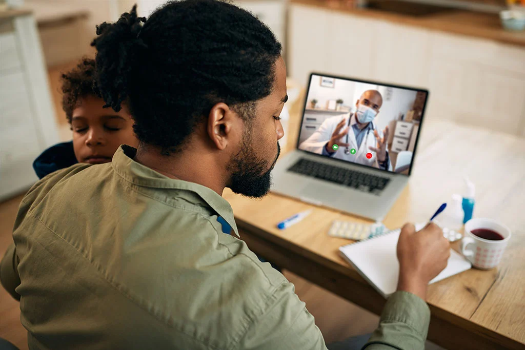 Man consulting with a doctor on laptop taking notes